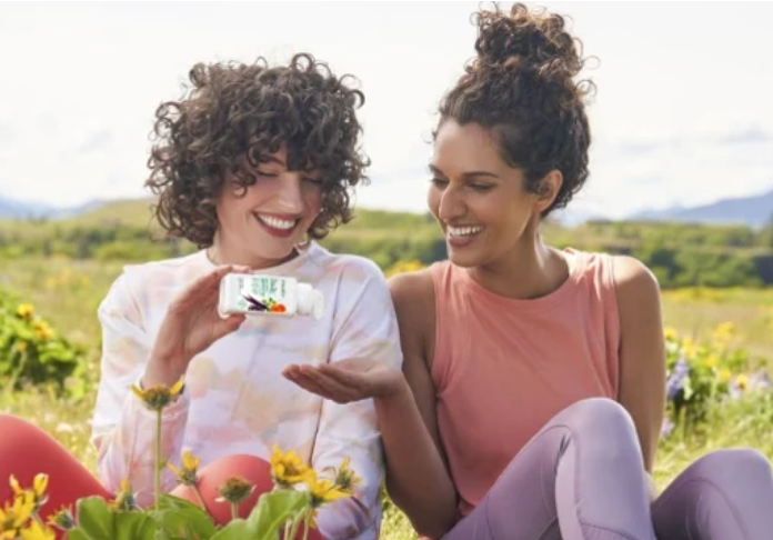 Due donne sorridenti con un integratore Nutrilite in un prato fiorito